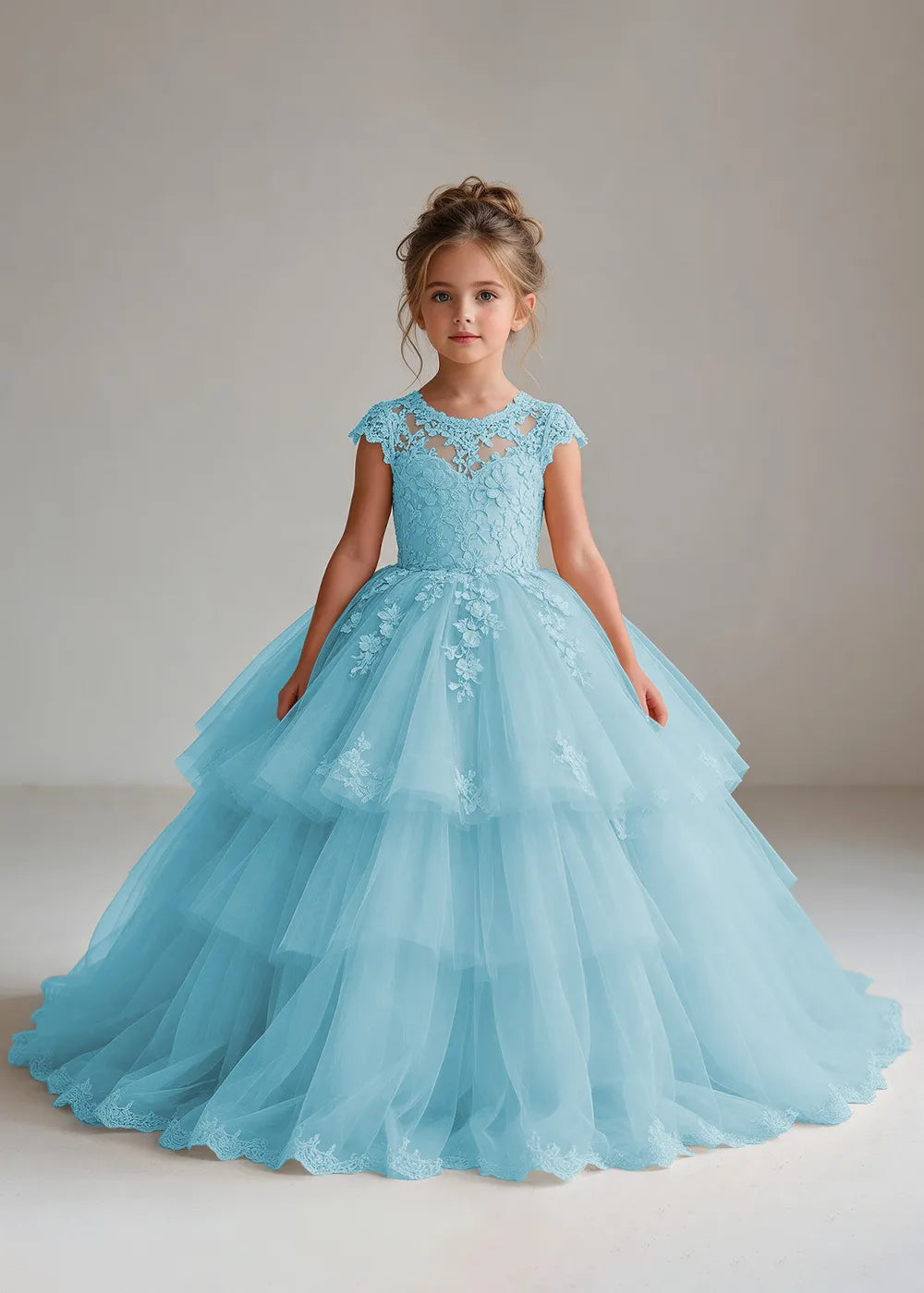 Front view of a child wearing a blue flower girl dress with a sheer lace illusion neckline, cap sleeves and a tiered cake-style tulle skirt with a lace-trimmed hem.