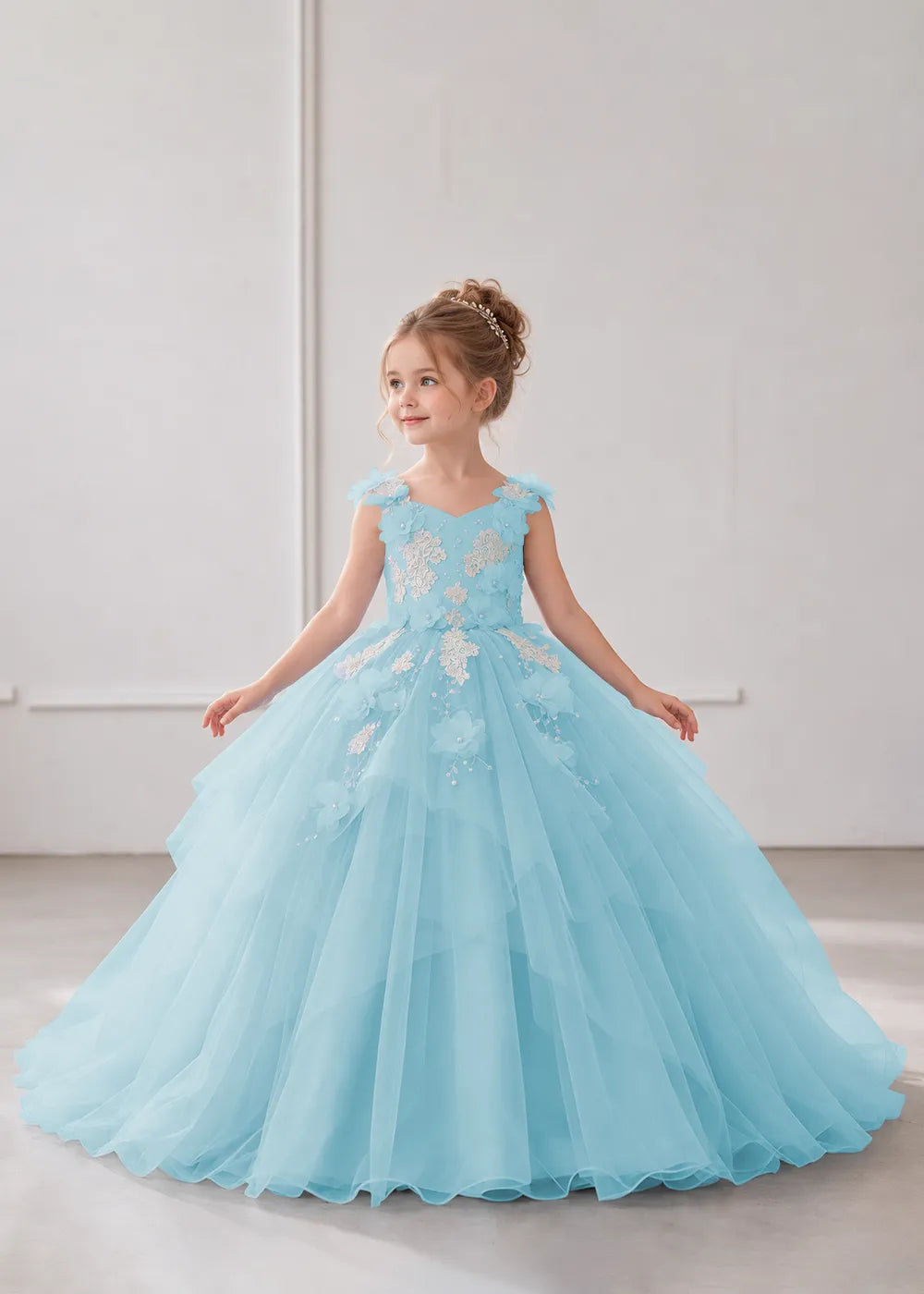 Front view of a child wearing a blue flower girl dress with a V-neckline, floral shoulder appliques and lace and flower decoration across the bodice and hips.