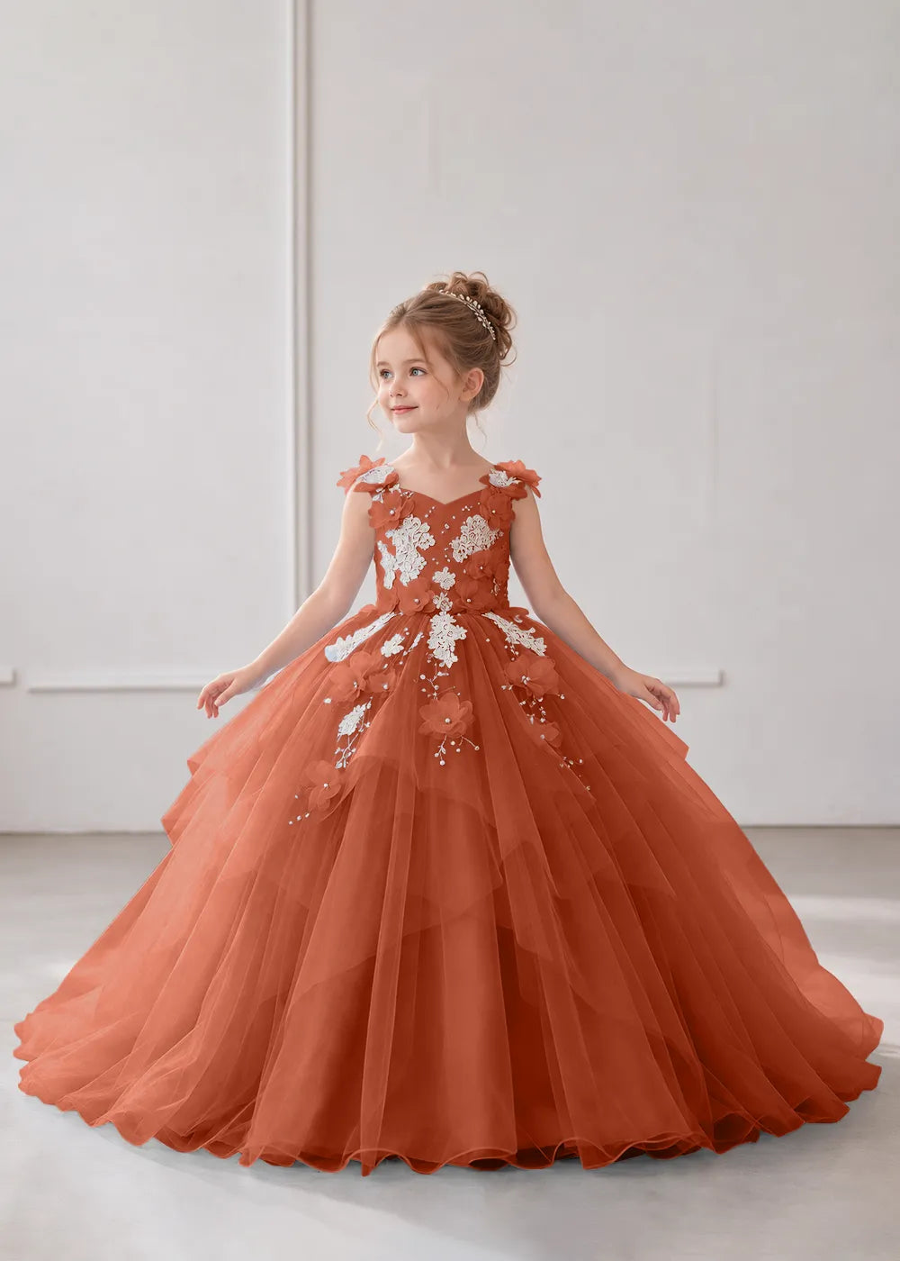 Front view of a child wearing a burnt orange flower girl dress with a V-neckline, floral shoulder appliques and lace and flower decoration across the bodice and hips.