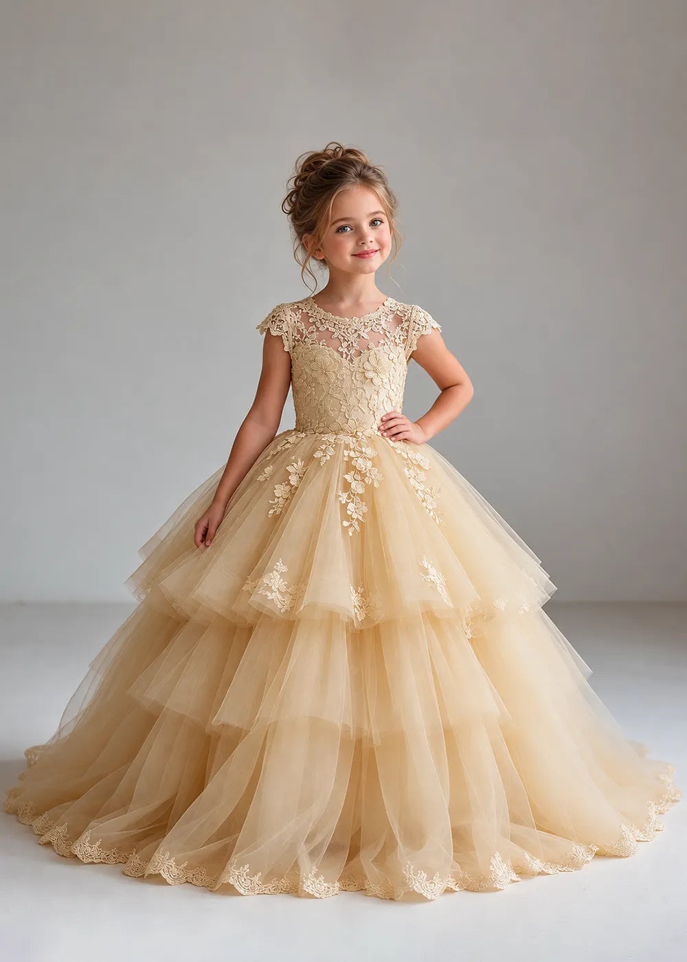 The three-quarter view of a child wearing a Champagne flower girl dress with a sheer lace illusion neckline, cap sleeves and a tiered cake-style tulle skirt with a lace-trimmed hem.