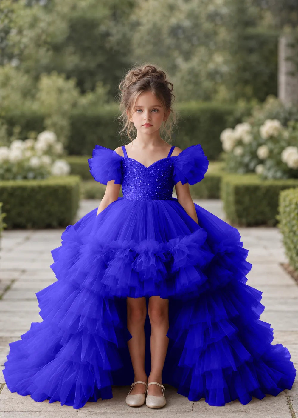 Front view of a child wearing a deep royal blue flower girl dress with a V-neckline, a sequin-covered bodice and a tiered high-low tulle skirt with off-shoulder sleeve ruffles.