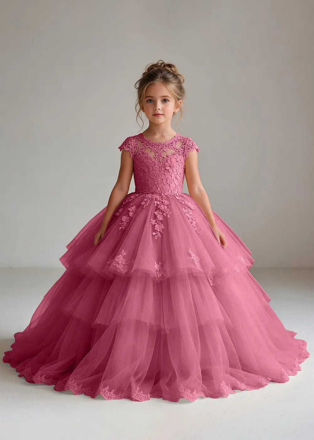 Front view of a child wearing a desert rose flower girl dress with a sheer lace illusion neckline, cap sleeves and a tiered cake-style tulle skirt with a lace-trimmed hem.
