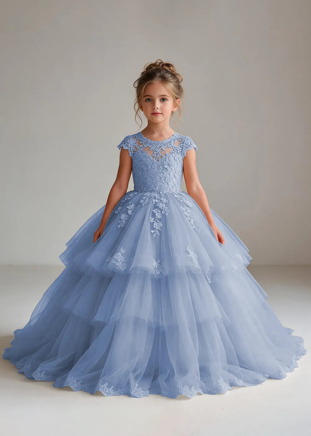 Front view of a child wearing a dusty blue flower girl dress with a sheer lace illusion neckline, cap sleeves and a tiered cake-style tulle skirt with a lace-trimmed hem.