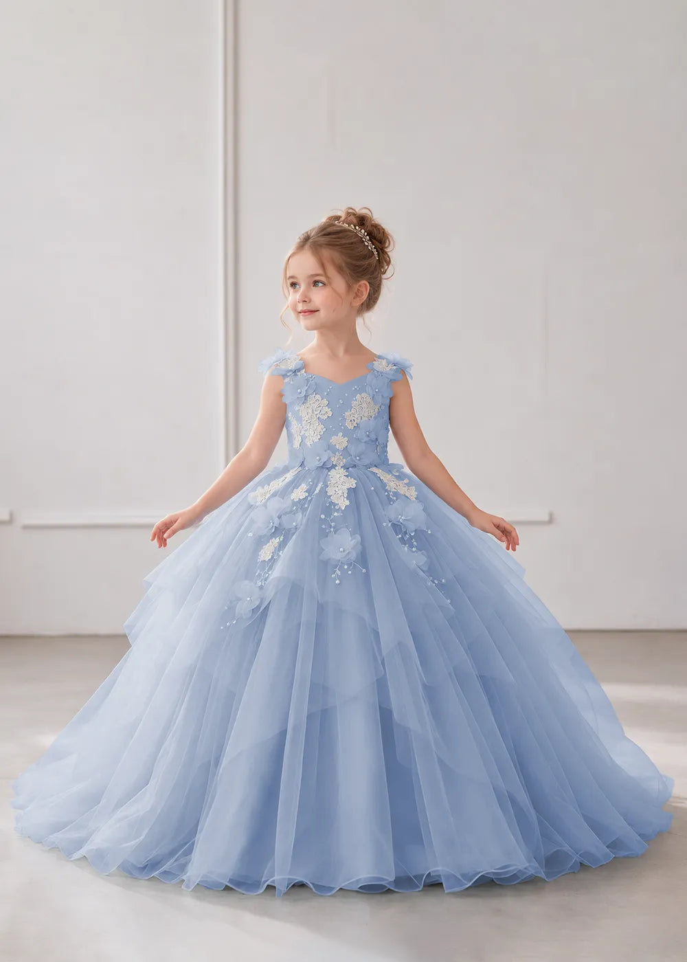 Front view of a child wearing a dusty blue flower girl dress with a V-neckline, floral shoulder appliques and lace and flower decoration across the bodice and hips.