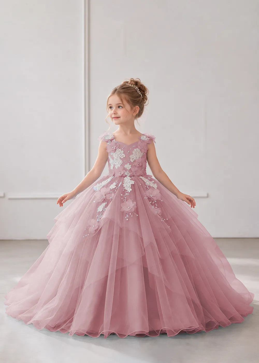 Front view of a child wearing a dusty rose flower girl dress with a V-neckline, floral shoulder appliques and lace and flower decoration across the bodice and hips.