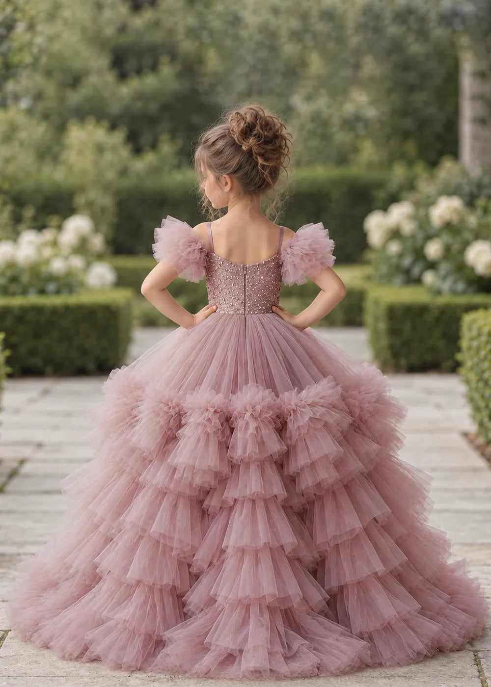 The rear view of a child wearing a Dusty Rose flower girl dress with a V-neckline, a sequin-covered bodice and a tiered high-low tulle skirt with off-shoulder sleeve ruffles.