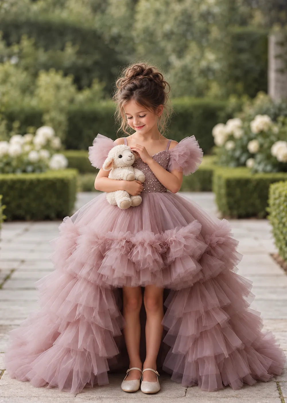 The three-quarter view of a child wearing a Dusty Rose flower girl dress with a V-neckline, a sequin-covered bodice and a tiered high-low tulle skirt with off-shoulder sleeve ruffles.
