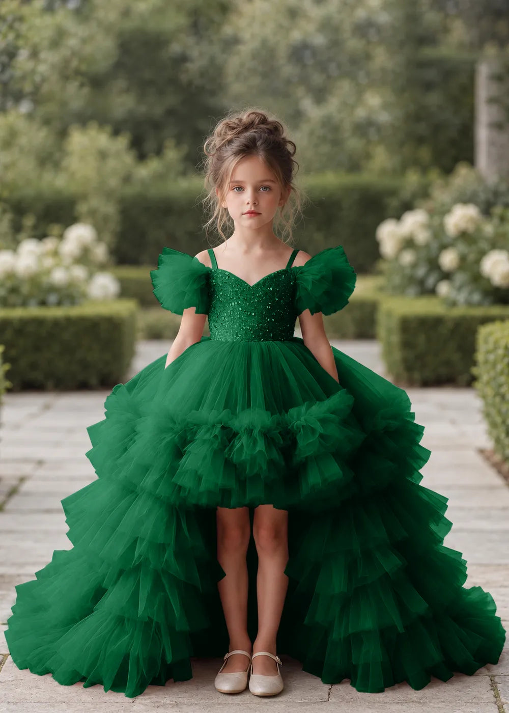 Front view of a child wearing a emerald green flower girl dress with a V-neckline, a sequin-covered bodice and a tiered high-low tulle skirt with off-shoulder sleeve ruffles.
