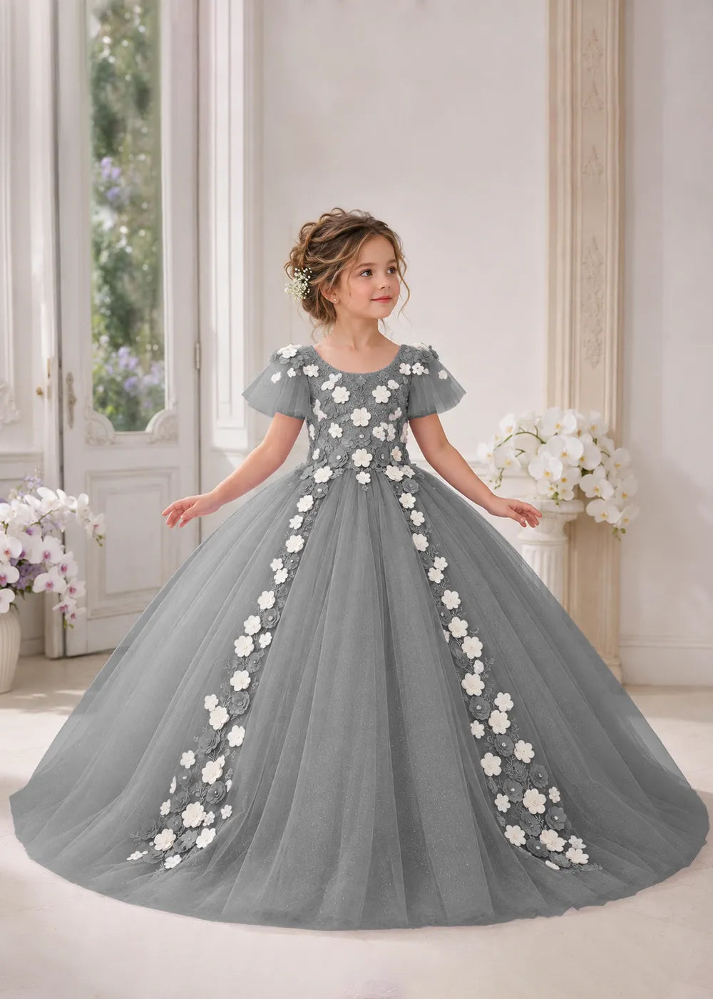 Front view of a child wearing a grey flower girl dress with a round neckline, sheer flutter cap sleeves and a floral vine cascading down both sides of a full tulle skirt.