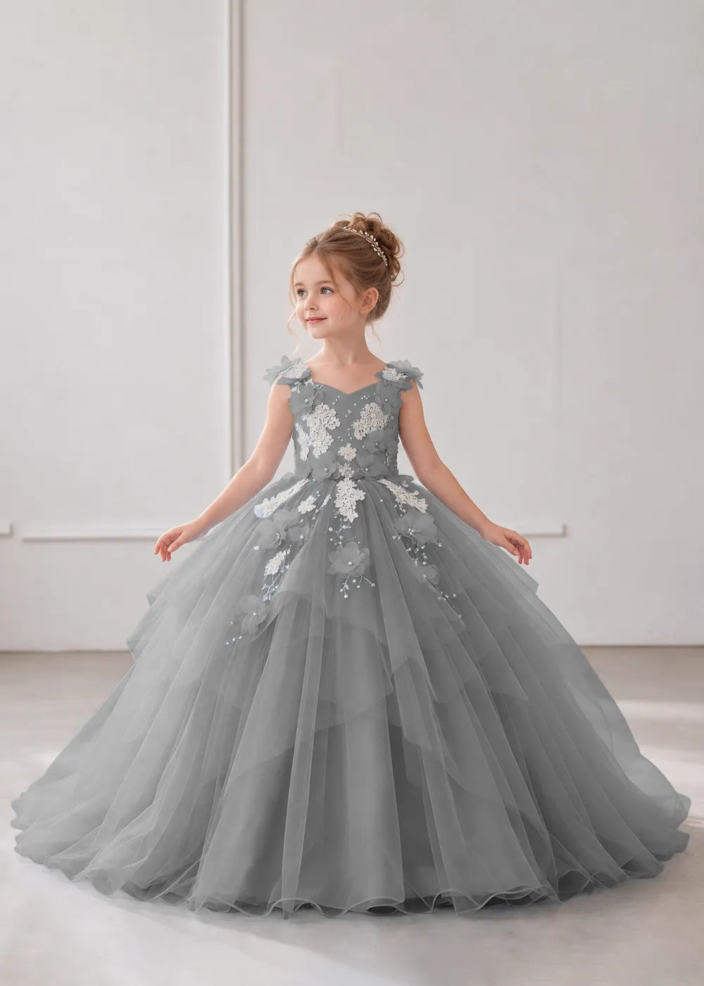 Front view of a child wearing a grey flower girl dress with a V-neckline, floral shoulder appliques and lace and flower decoration across the bodice and hips.