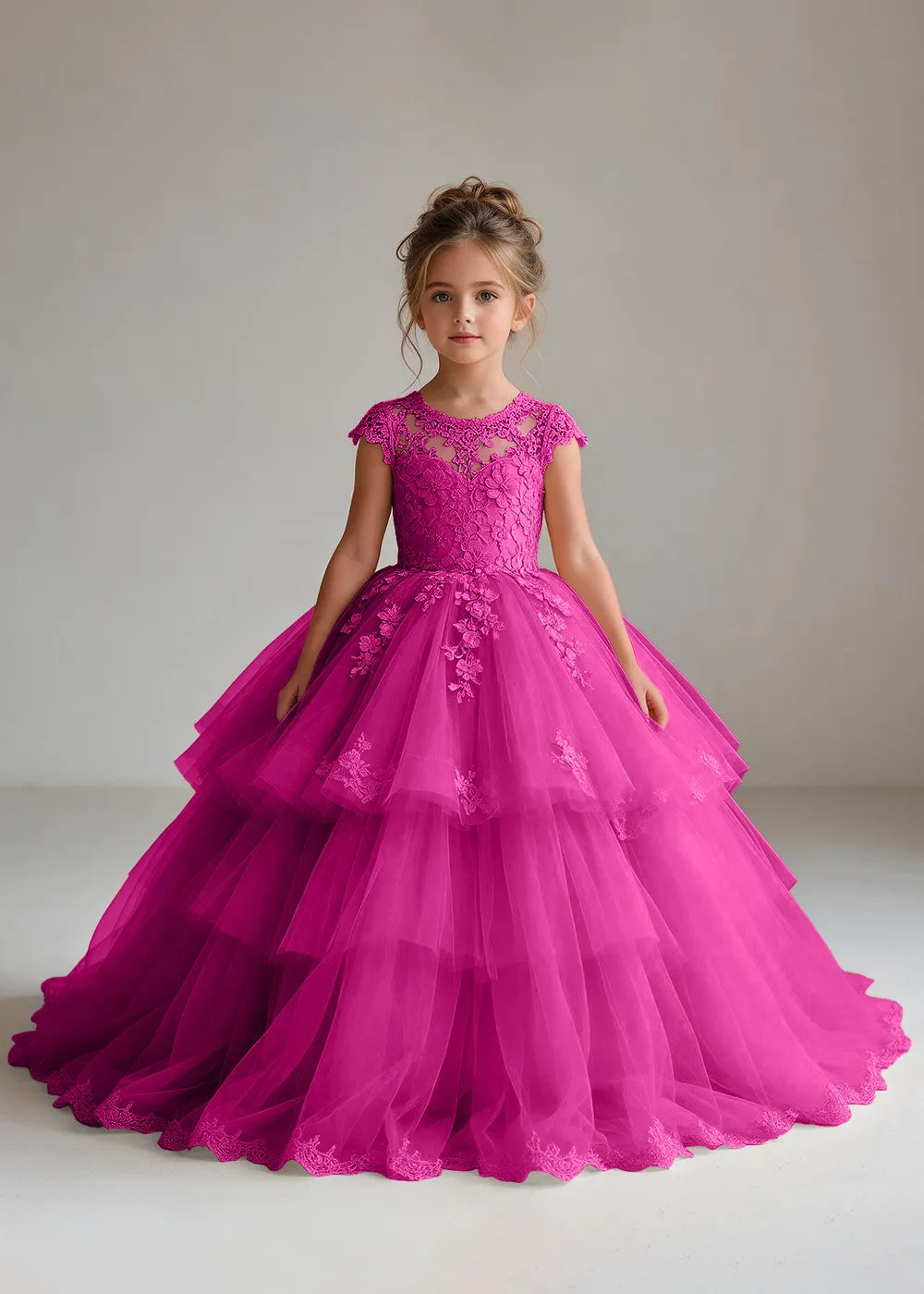 Front view of a child wearing a hot pink flower girl dress with a sheer lace illusion neckline, cap sleeves and a tiered cake-style tulle skirt with a lace-trimmed hem.