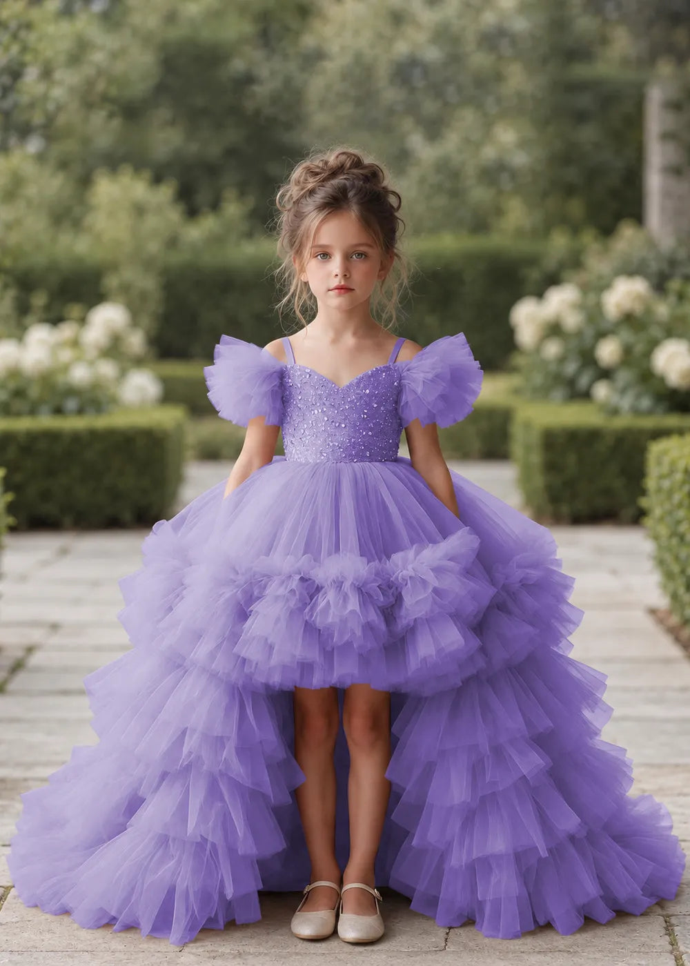 Front view of a child wearing a lavender flower girl dress with a V-neckline, a sequin-covered bodice and a tiered high-low tulle skirt with off-shoulder sleeve ruffles.