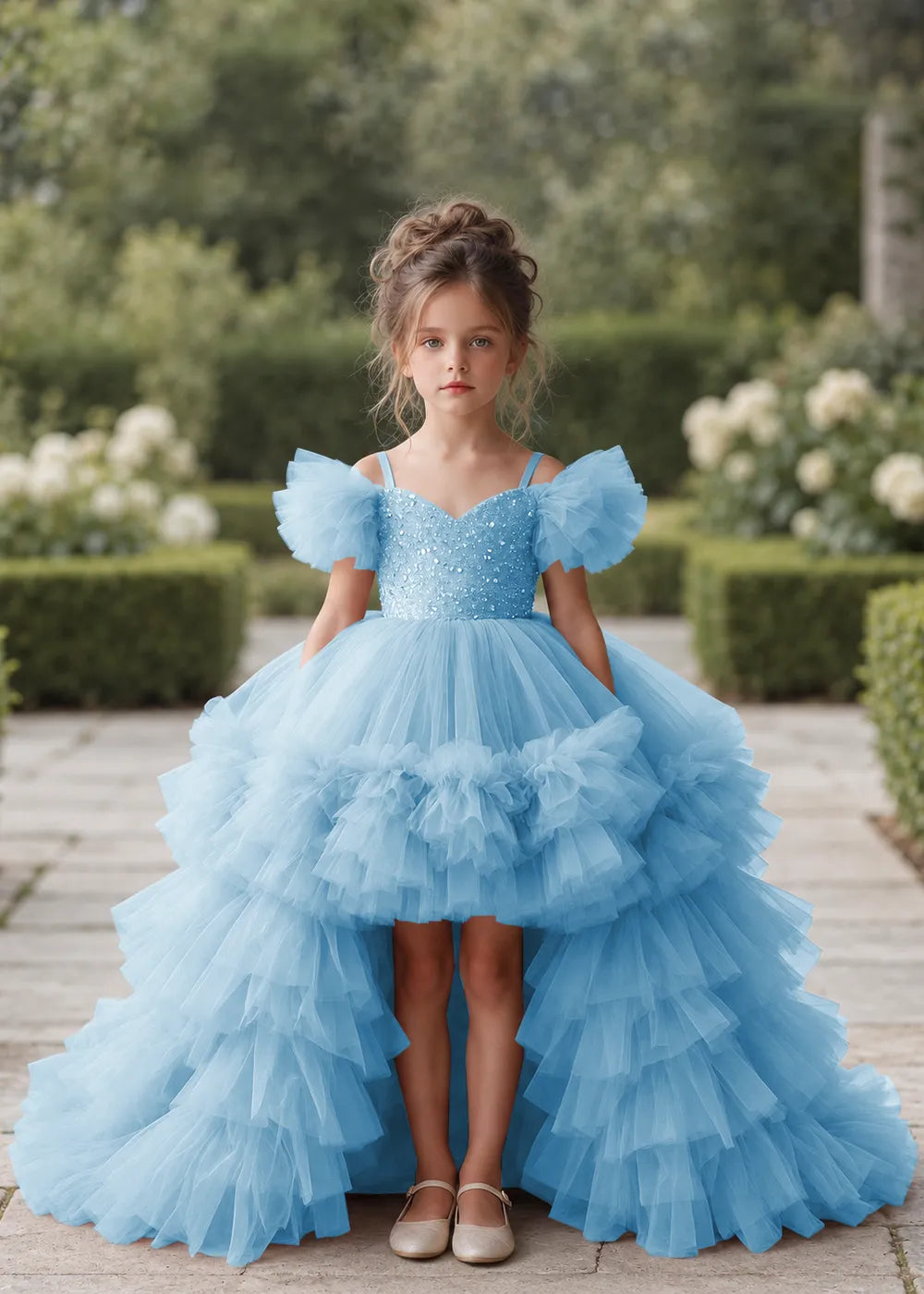 Front view of a child wearing a light blue flower girl dress with a V-neckline, a sequin-covered bodice and a tiered high-low tulle skirt with off-shoulder sleeve ruffles.