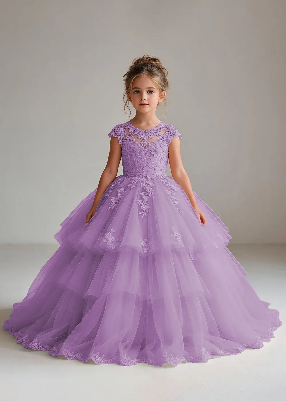 Front view of a child wearing a lilac flower girl dress with a sheer lace illusion neckline, cap sleeves and a tiered cake-style tulle skirt with a lace-trimmed hem.