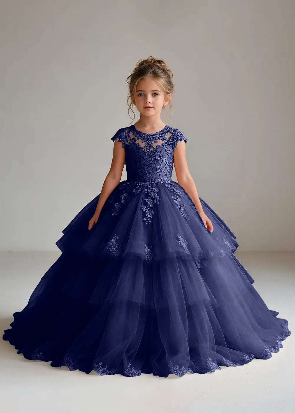 Front view of a child wearing a navy blue flower girl dress with a sheer lace illusion neckline, cap sleeves and a tiered cake-style tulle skirt with a lace-trimmed hem.