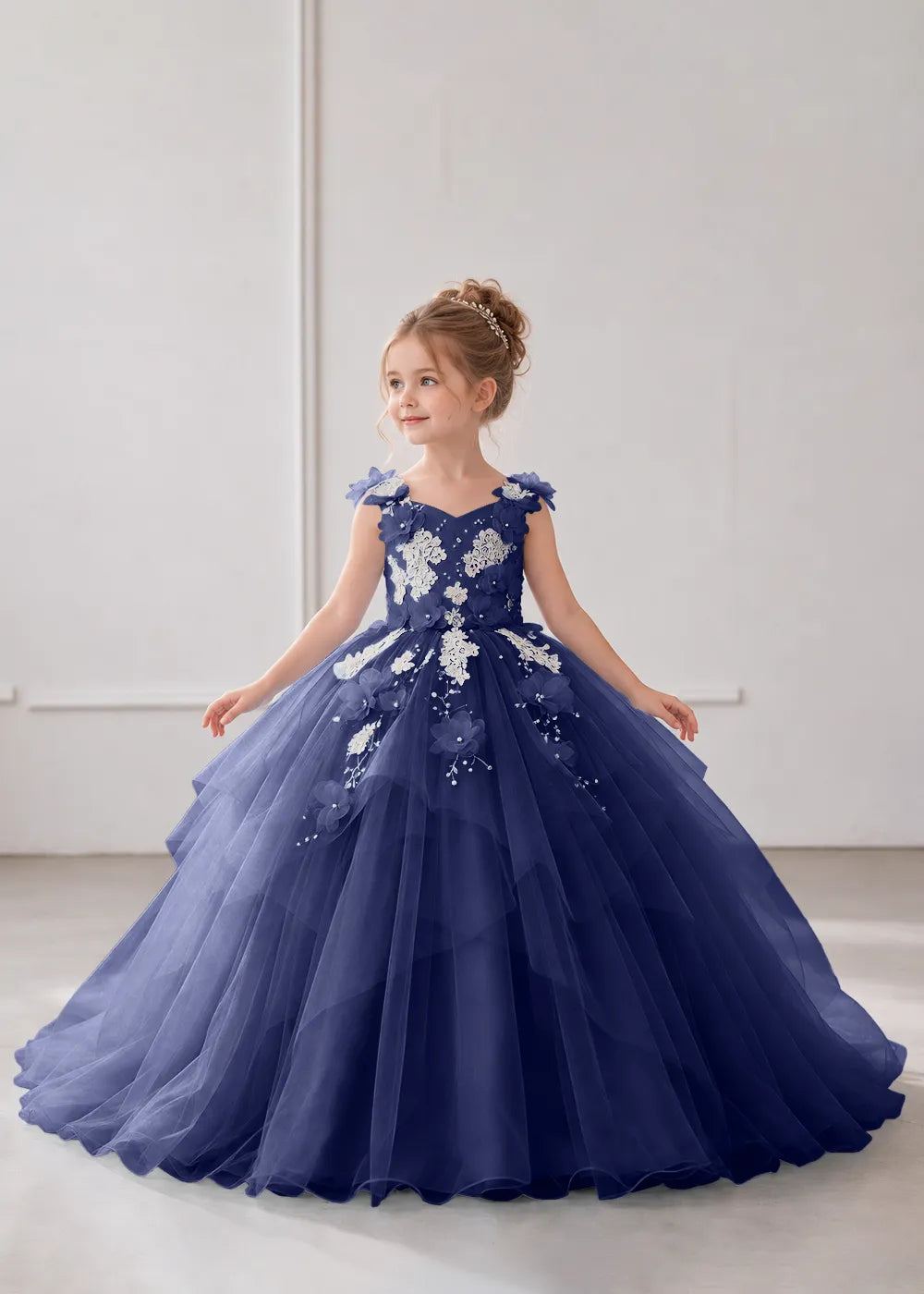 Front view of a child wearing a navy blue flower girl dress with a V-neckline, floral shoulder appliques and lace and flower decoration across the bodice and hips.