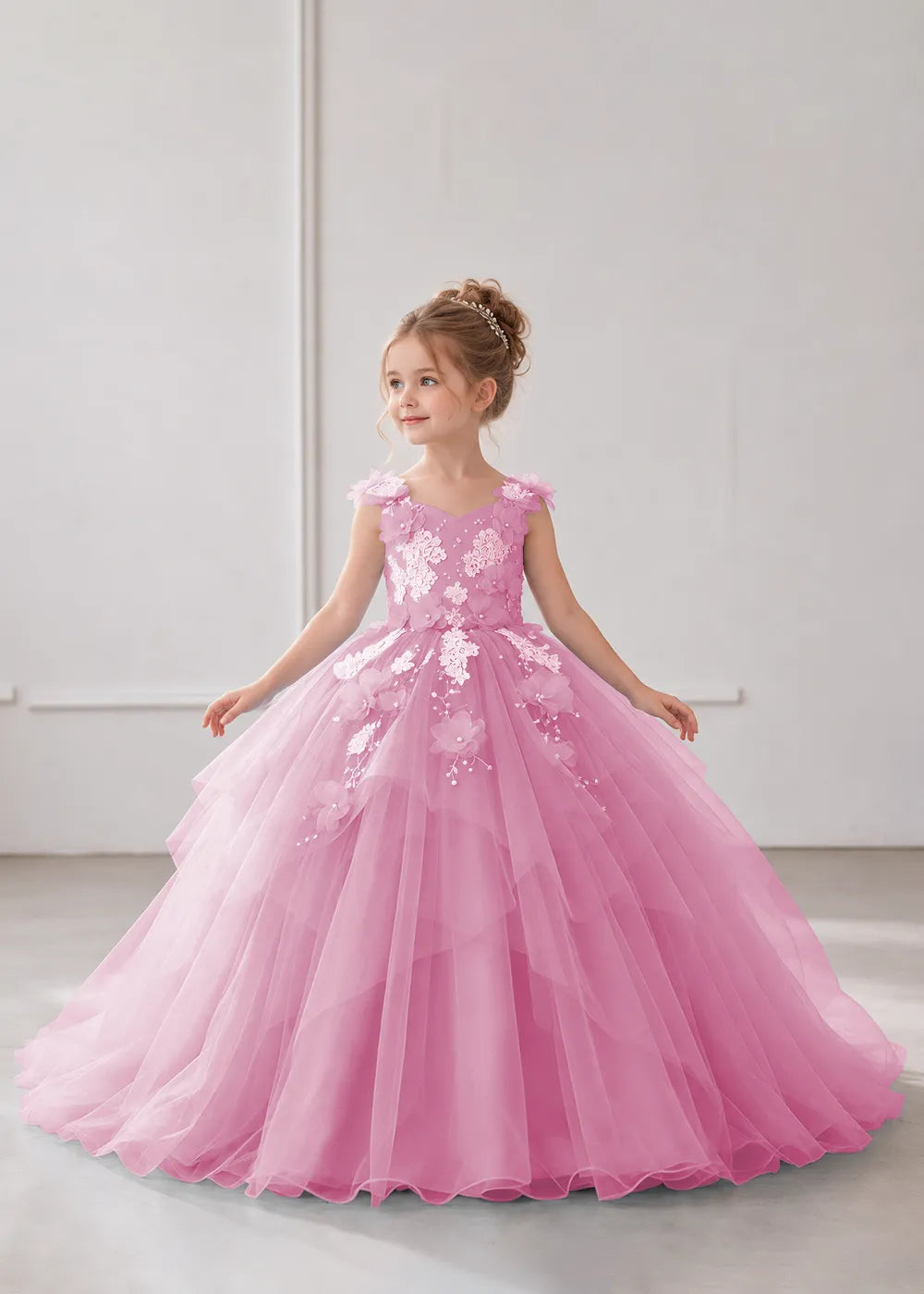 Front view of a child wearing a pearl pink flower girl dress with a V-neckline, floral shoulder appliques and lace and flower decoration across the bodice and hips.
