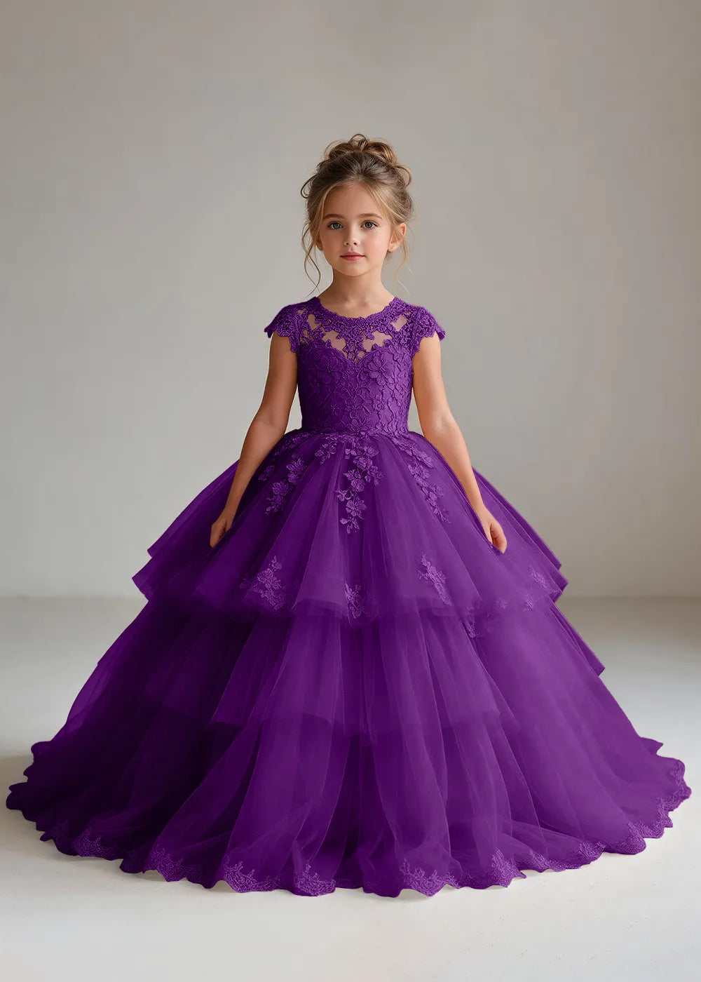 Front view of a child wearing a purple flower girl dress with a sheer lace illusion neckline, cap sleeves and a tiered cake-style tulle skirt with a lace-trimmed hem.