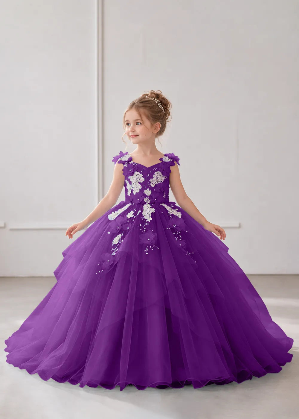 Front view of a child wearing a purple flower girl dress with a V-neckline, floral shoulder appliques and lace and flower decoration across the bodice and hips.