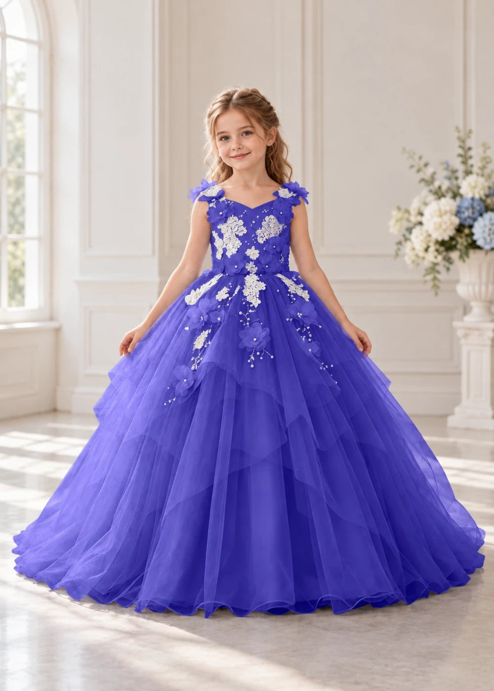 Front view of a child wearing a royal blue flower girl dress with a V-neckline, floral shoulder appliques and lace and flower decoration across the bodice and hips.