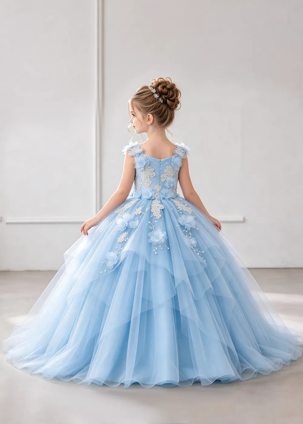 The rear view of a child wearing a Sky Blue flower girl dress with a V-neckline, floral shoulder appliques and lace and flower decoration across the bodice and hips.