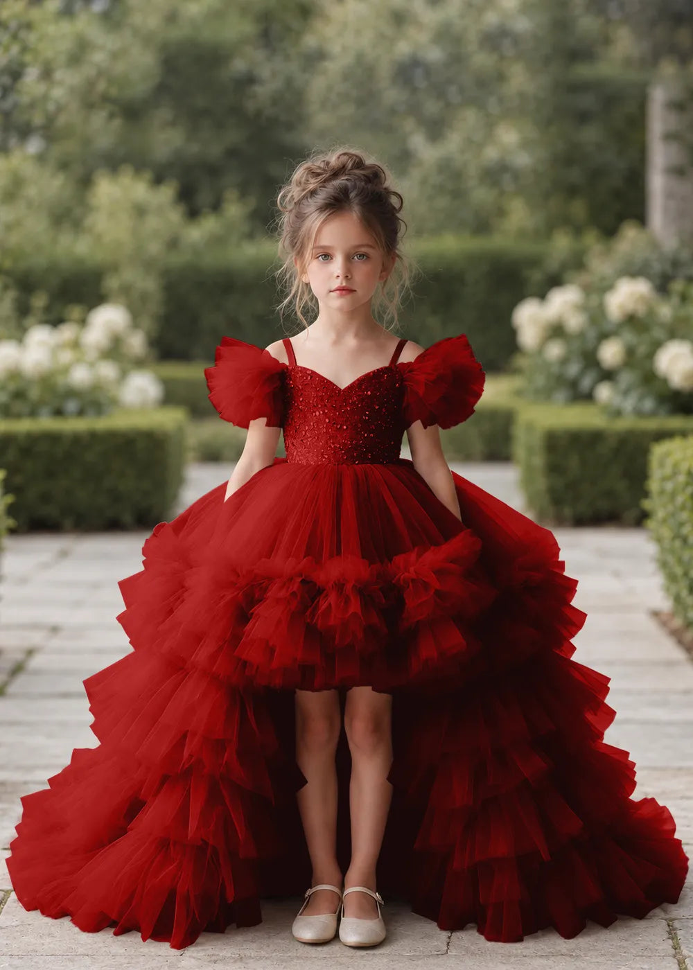 Front view of a child wearing a wine red flower girl dress with a V-neckline, a sequin-covered bodice and a tiered high-low tulle skirt with off-shoulder sleeve ruffles.