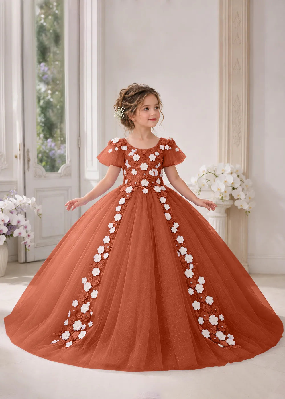 Front view of a child wearing a burnt orange flower girl dress with a round neckline, sheer flutter cap sleeves and a floral vine cascading down both sides of a full tulle skirt.