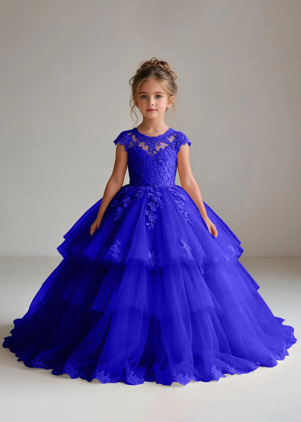 Front view of a child wearing a deep royal blue flower girl dress with a sheer lace illusion neckline, cap sleeves and a tiered cake-style tulle skirt with a lace-trimmed hem.