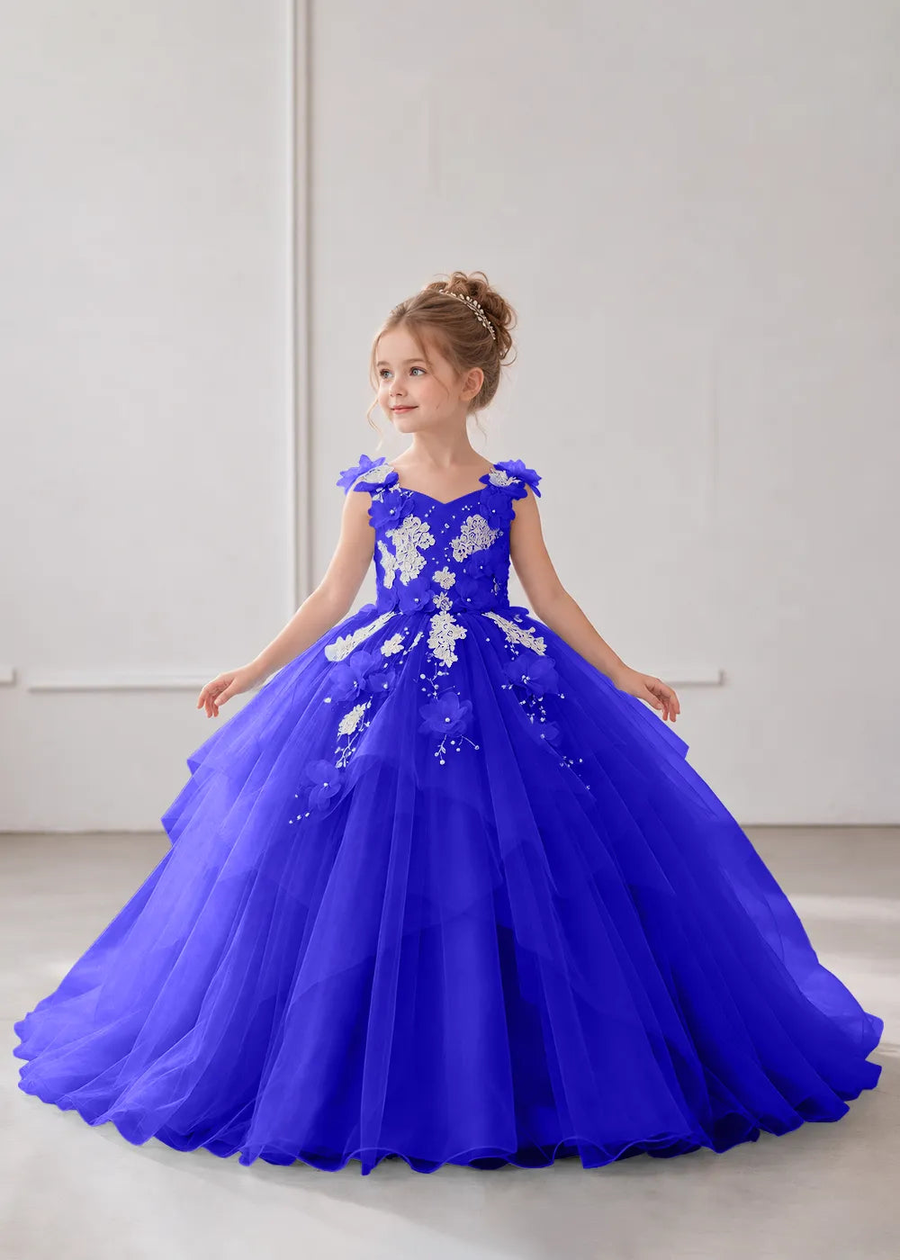Front view of a child wearing a deep royal blue flower girl dress with a V-neckline, floral shoulder appliques and lace and flower decoration across the bodice and hips.