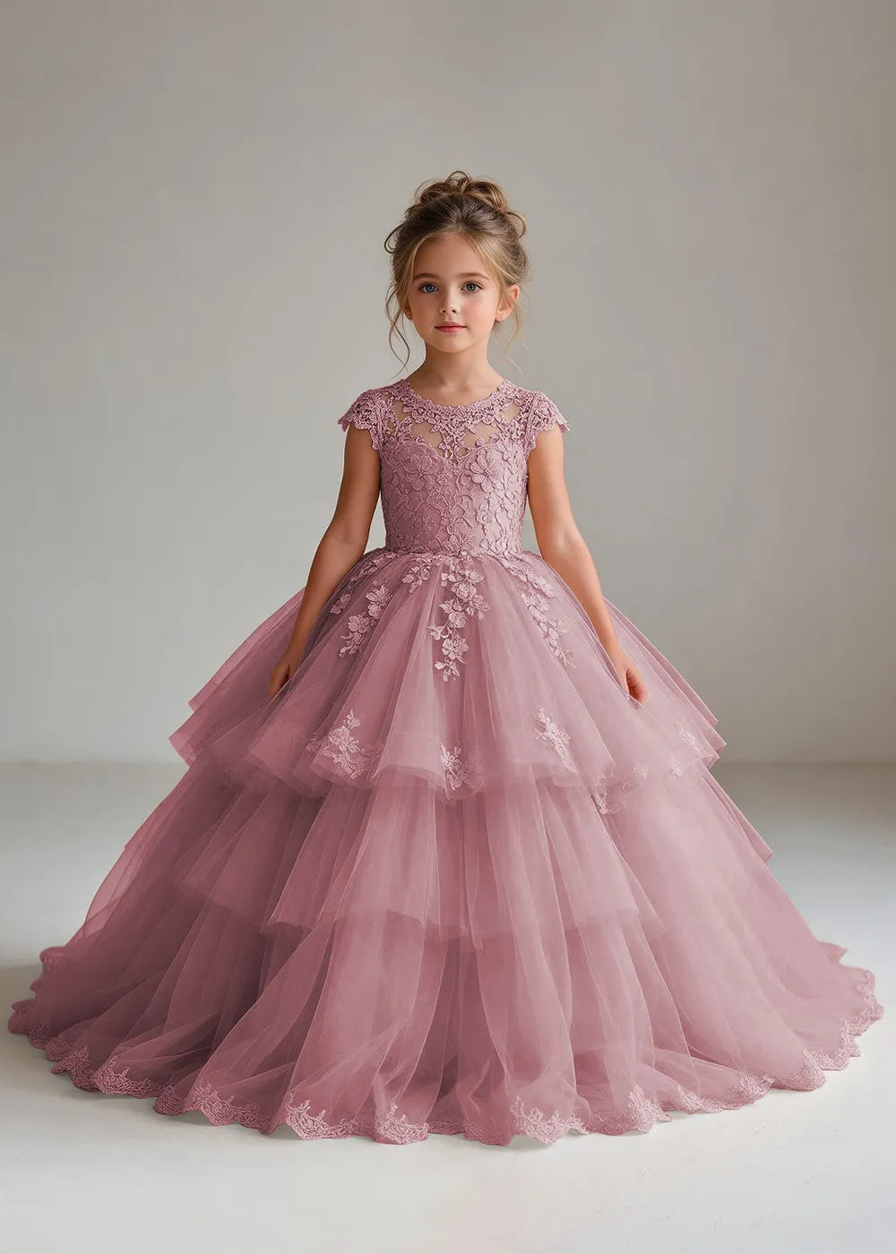Front view of a child wearing a dusty rose flower girl dress with a sheer lace illusion neckline, cap sleeves and a tiered cake-style tulle skirt with a lace-trimmed hem.