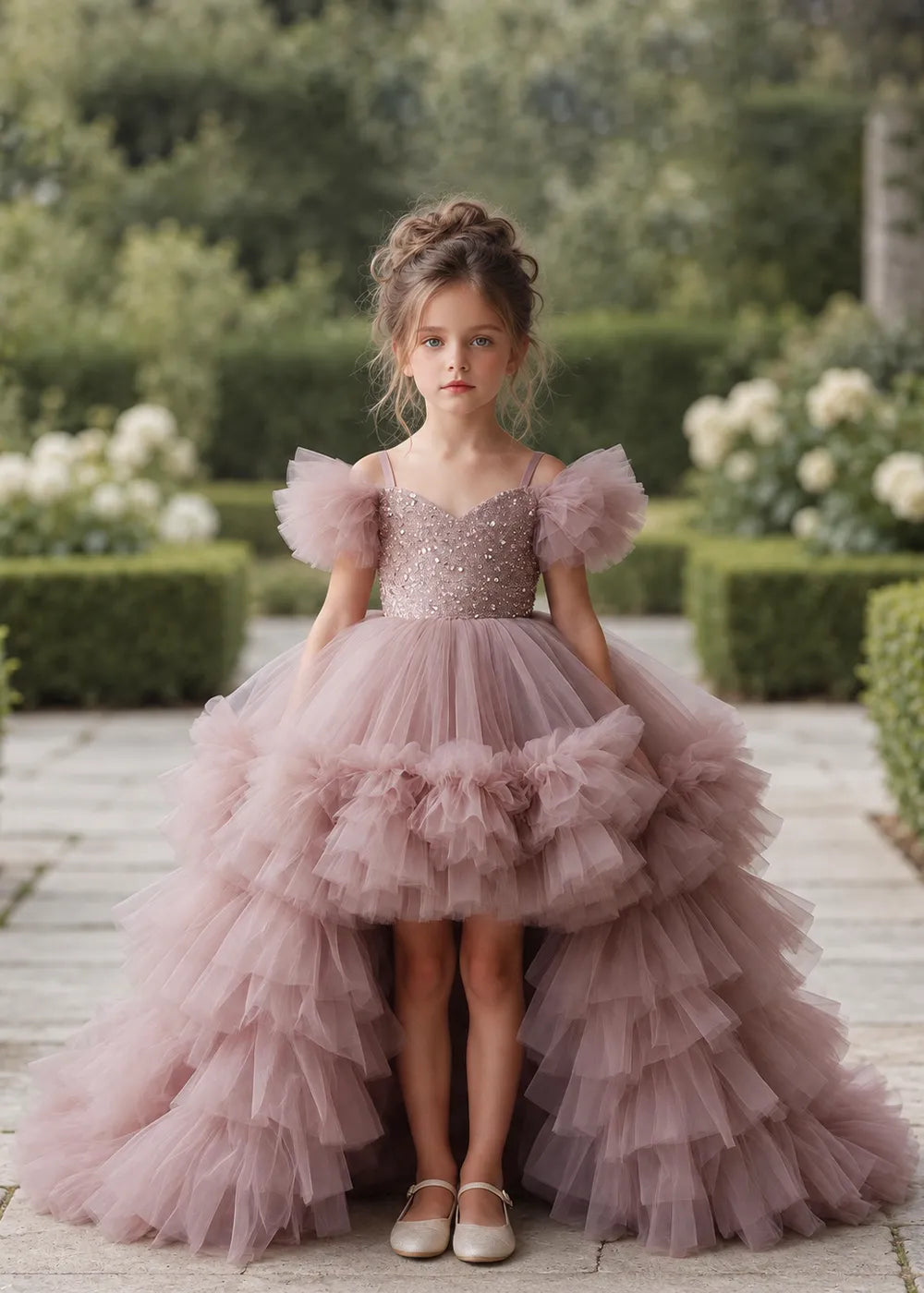 The front view of a child wearing a Dusty Rose flower girl dress with a V-neckline, a sequin-covered bodice and a tiered high-low tulle skirt with off-shoulder sleeve ruffles.