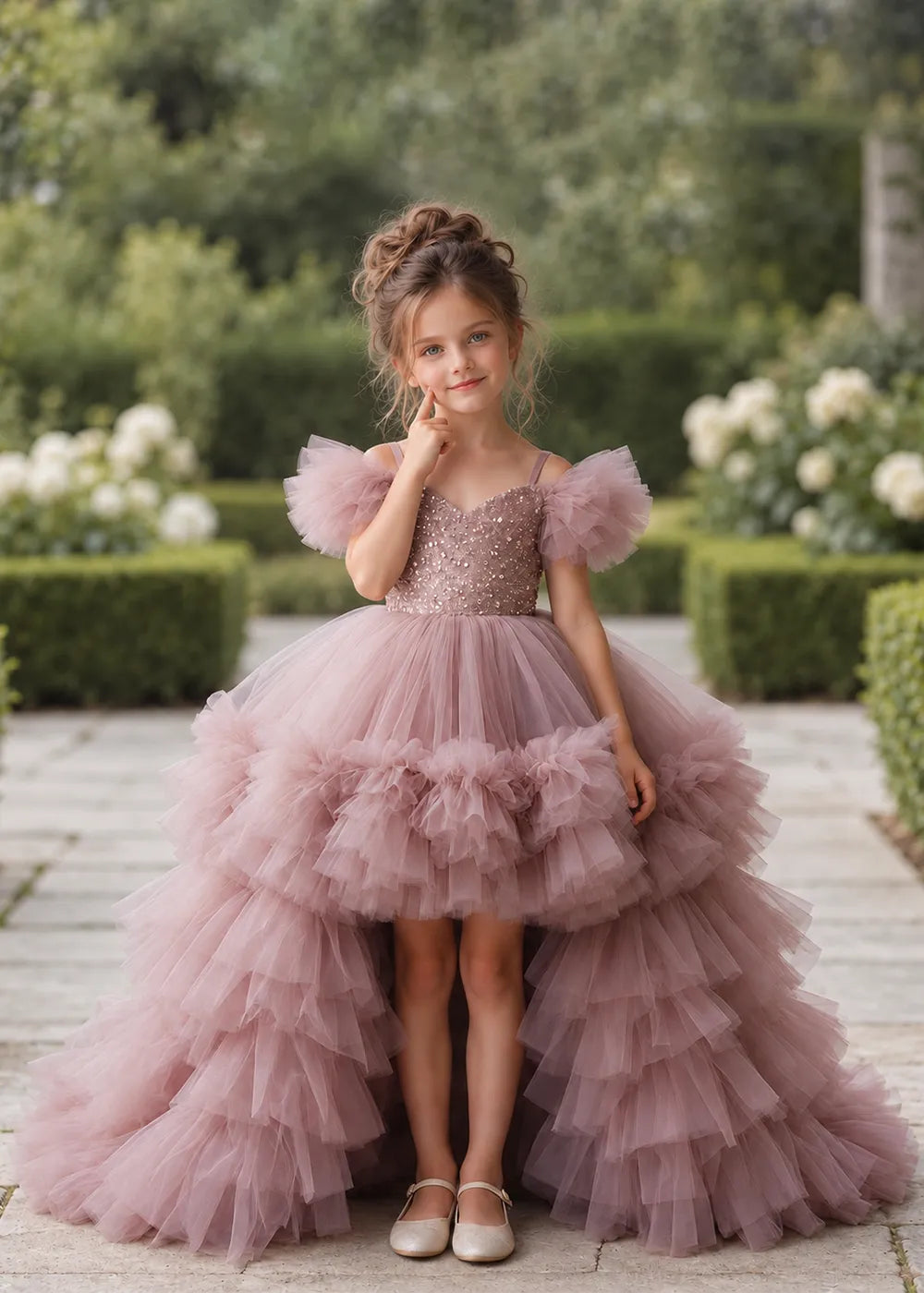 The front view of a child wearing a Dusty Rose flower girl dress with a V-neckline, a sequin-covered bodice and a tiered high-low tulle skirt with off-shoulder sleeve ruffles.
