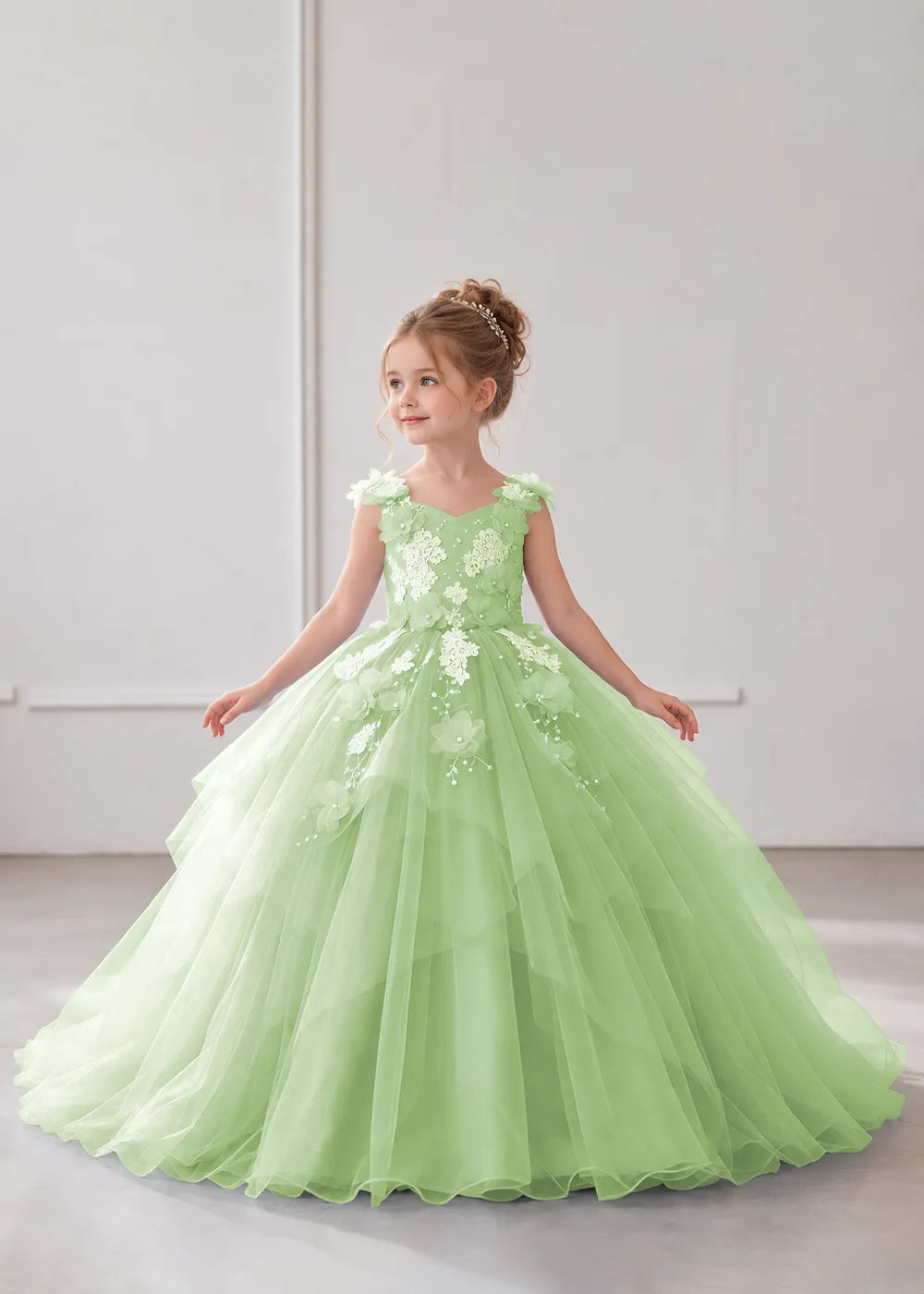 Front view of a child wearing a dusty sage flower girl dress with a V-neckline, floral shoulder appliques and lace and flower decoration across the bodice and hips.