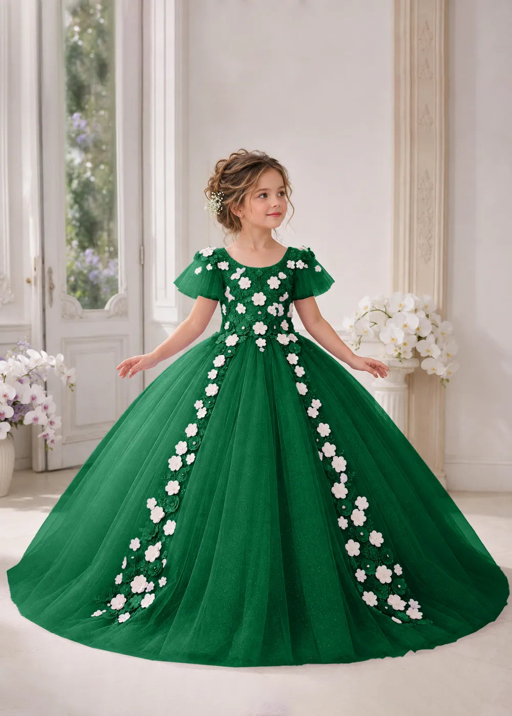 Front view of a child wearing a emerald green flower girl dress with a round neckline, sheer flutter cap sleeves and a floral vine cascading down both sides of a full tulle skirt.