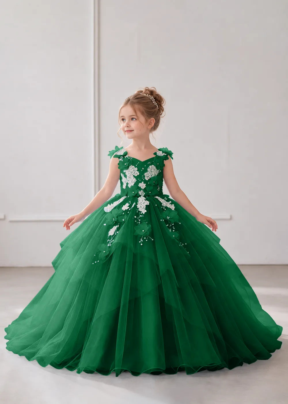 Front view of a child wearing a emerald green flower girl dress with a V-neckline, floral shoulder appliques and lace and flower decoration across the bodice and hips.