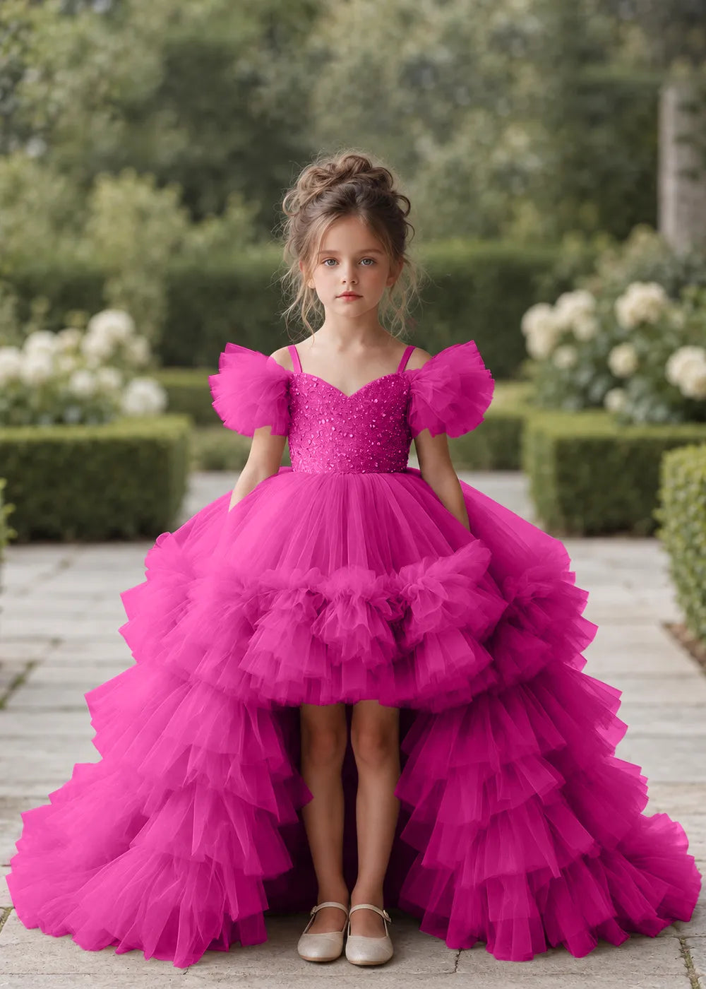 Front view of a child wearing a hot pink flower girl dress with a V-neckline, a sequin-covered bodice and a tiered high-low tulle skirt with off-shoulder sleeve ruffles.