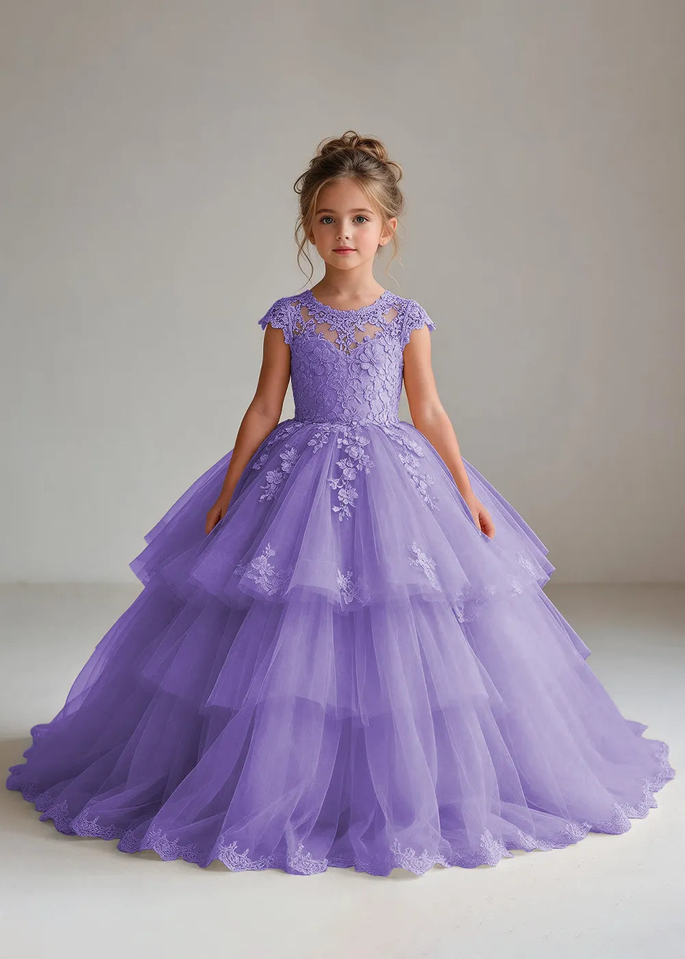 Front view of a child wearing a lavender flower girl dress with a sheer lace illusion neckline, cap sleeves and a tiered cake-style tulle skirt with a lace-trimmed hem.