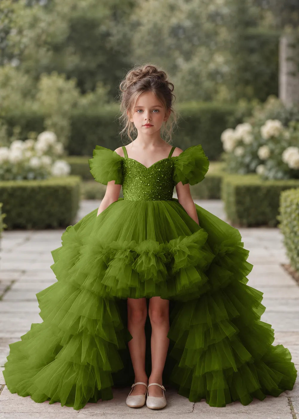 Front view of a child wearing a olive flower girl dress with a V-neckline, a sequin-covered bodice and a tiered high-low tulle skirt with off-shoulder sleeve ruffles.