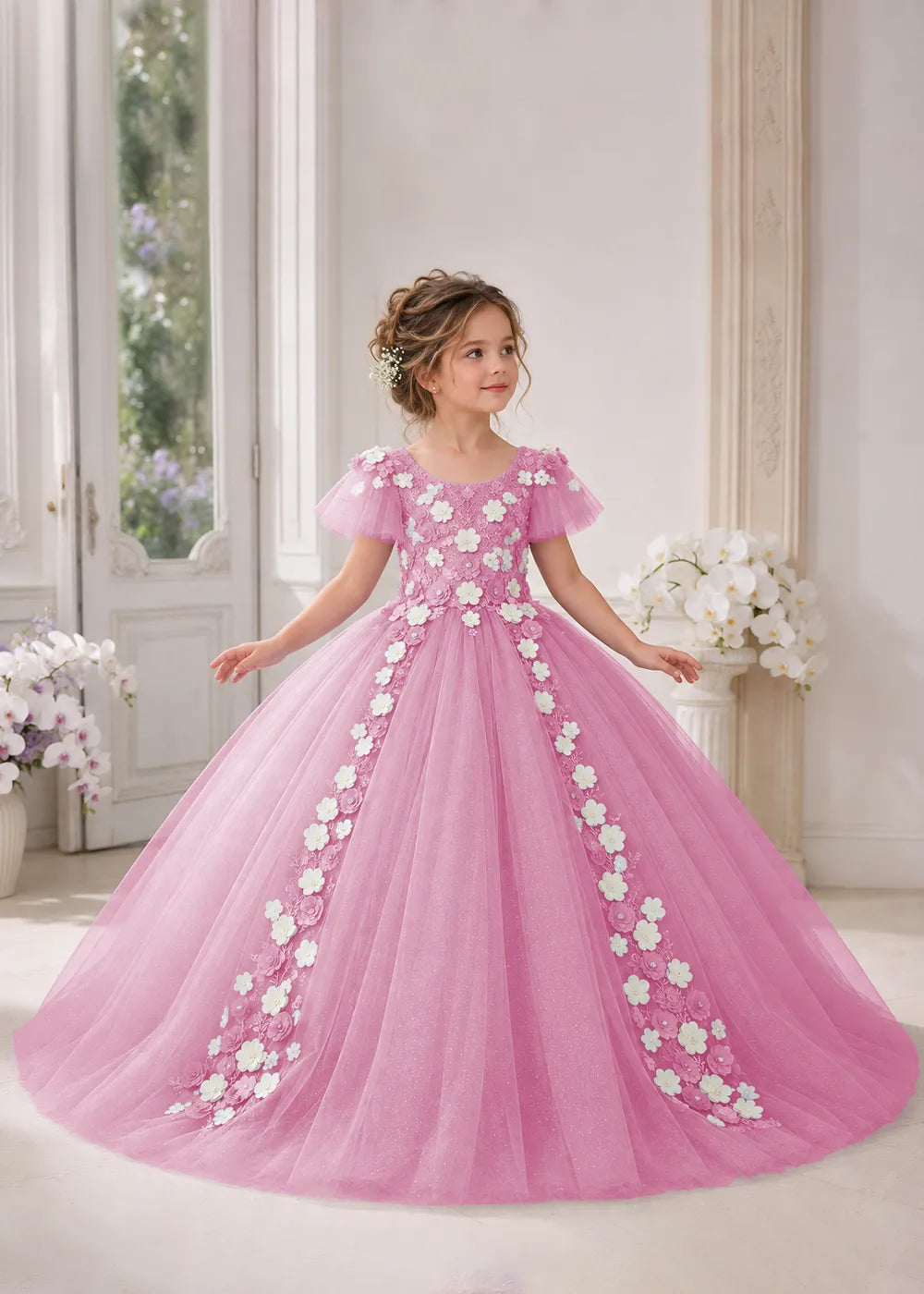 Front view of a child wearing a pearl pink flower girl dress with a round neckline, sheer flutter cap sleeves and a floral vine cascading down both sides of a full tulle skirt.