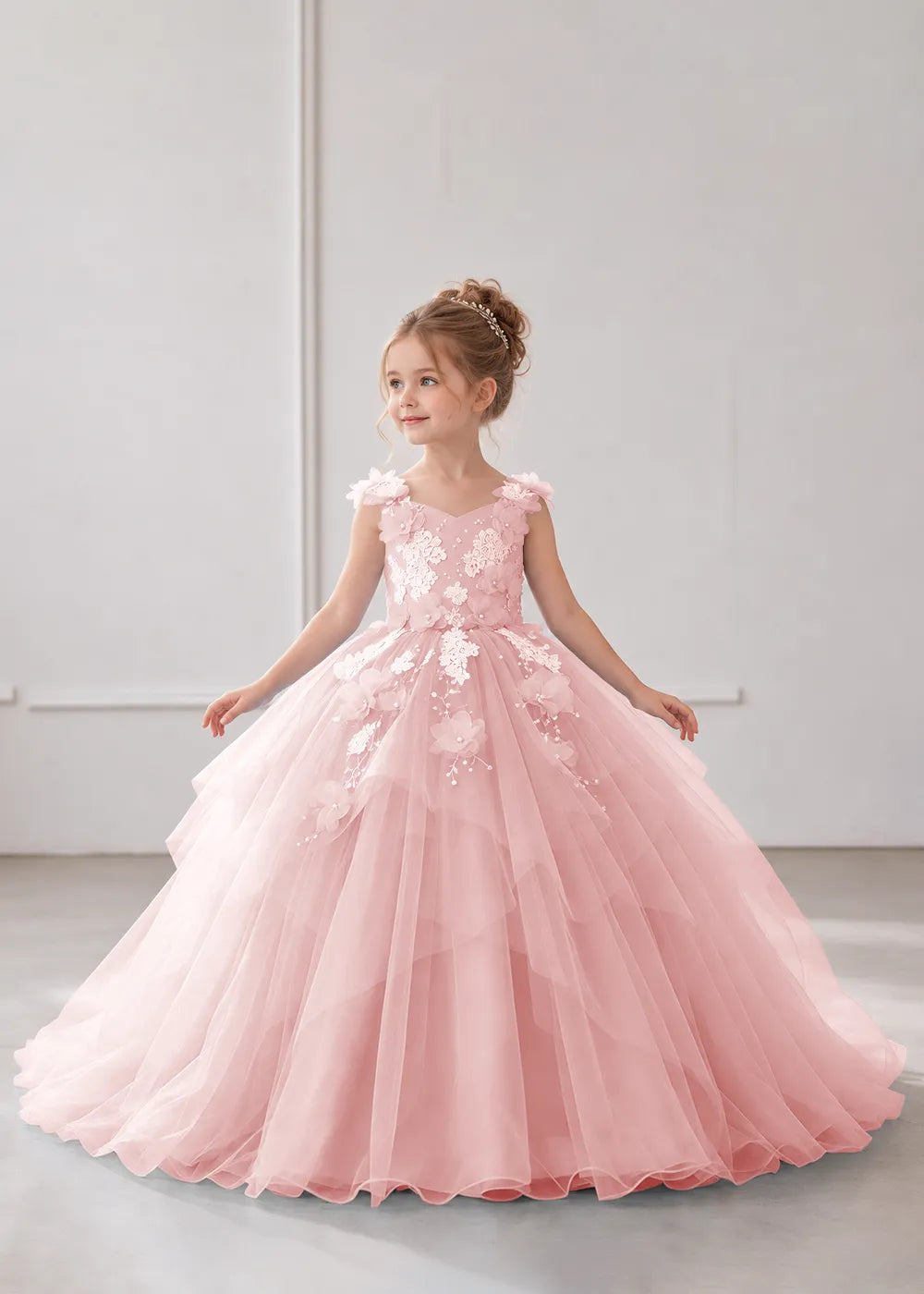 Front view of a child wearing a pink flower girl dress with a V-neckline, floral shoulder appliques and lace and flower decoration across the bodice and hips.