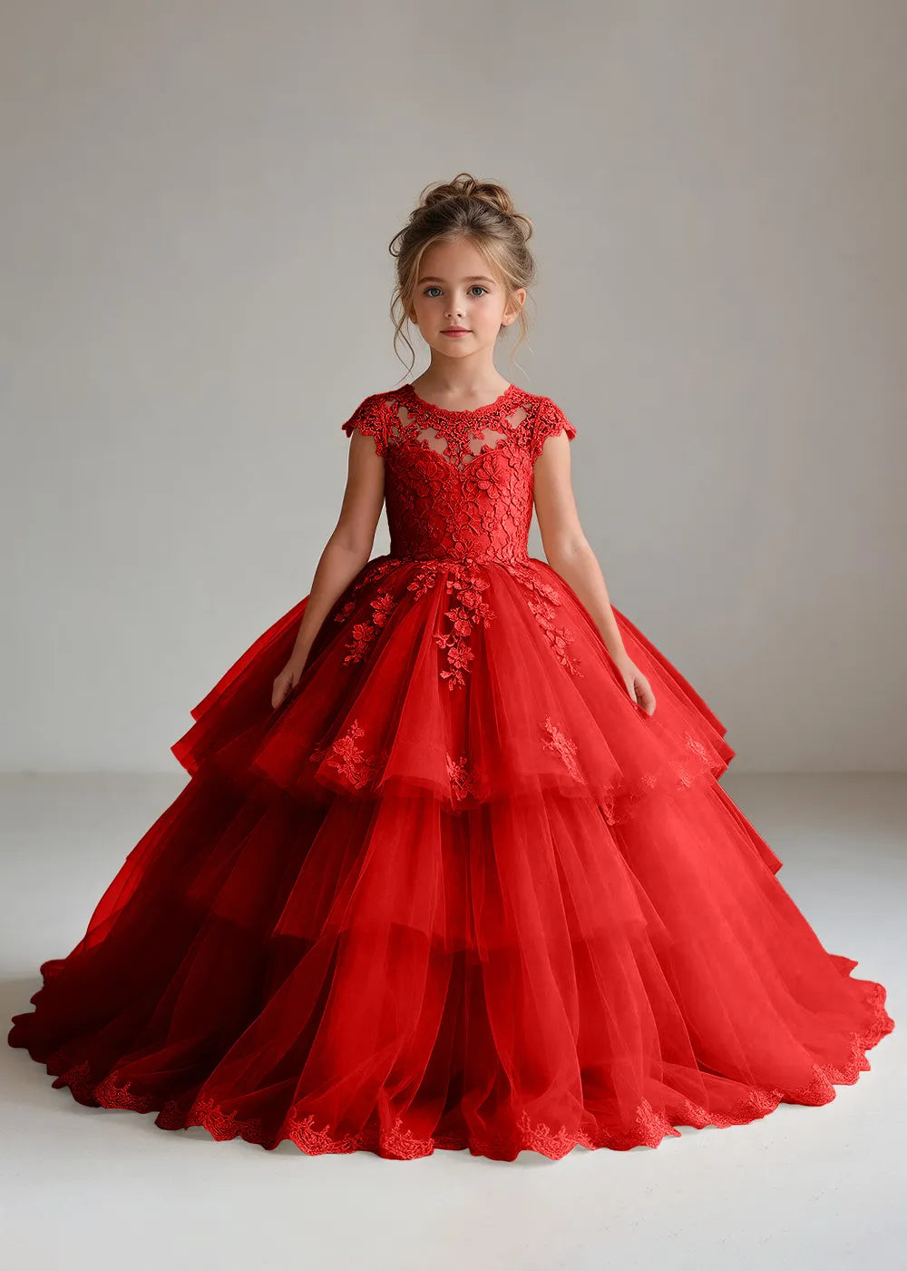 Front view of a child wearing a red flower girl dress with a sheer lace illusion neckline, cap sleeves and a tiered cake-style tulle skirt with a lace-trimmed hem.