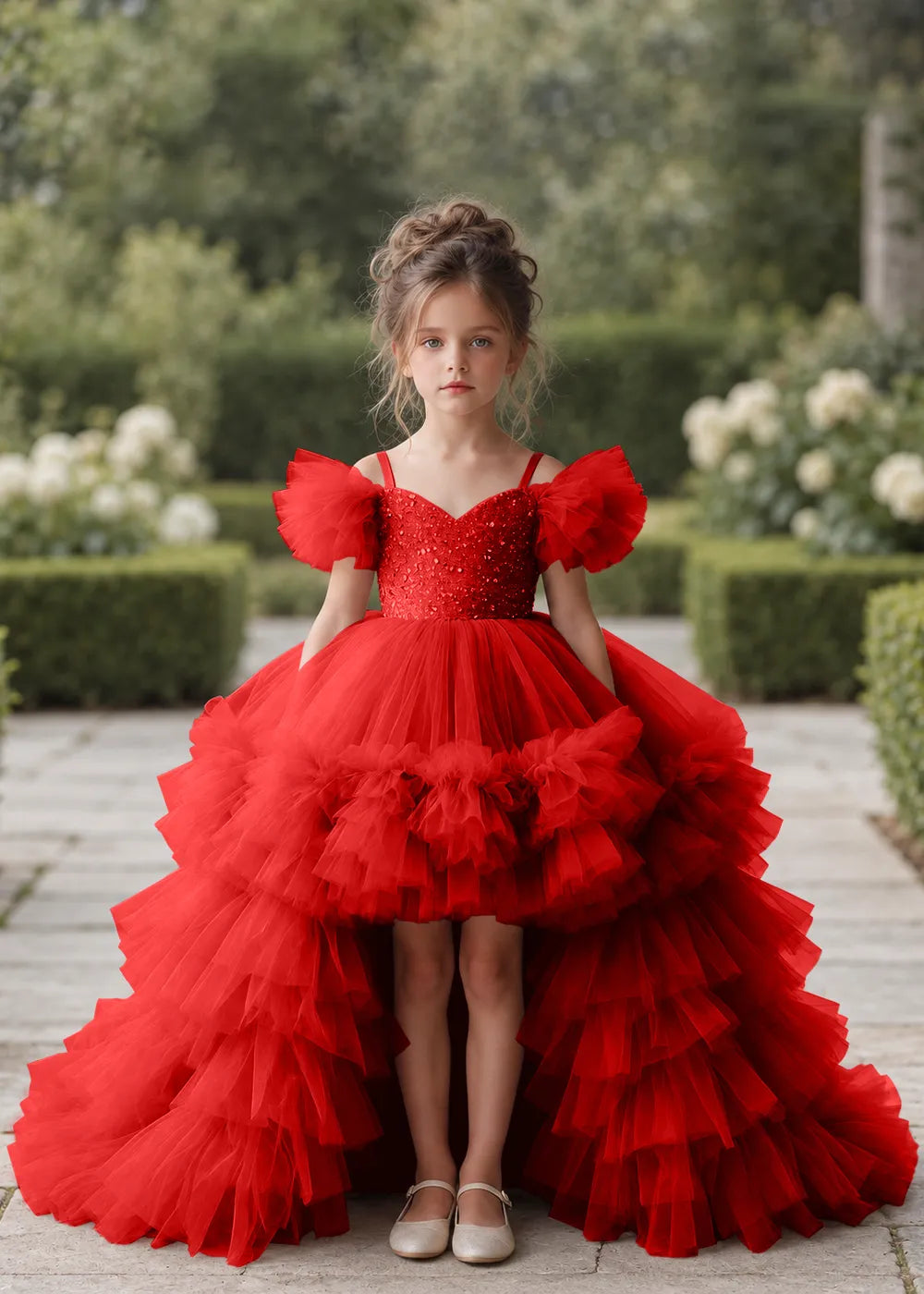 Front view of a child wearing a red flower girl dress with a V-neckline, a sequin-covered bodice and a tiered high-low tulle skirt with off-shoulder sleeve ruffles.