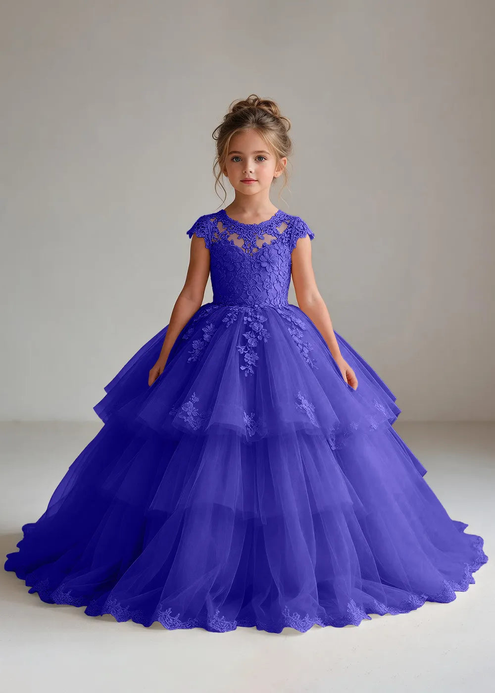 Front view of a child wearing a royal blue flower girl dress with a sheer lace illusion neckline, cap sleeves and a tiered cake-style tulle skirt with a lace-trimmed hem.