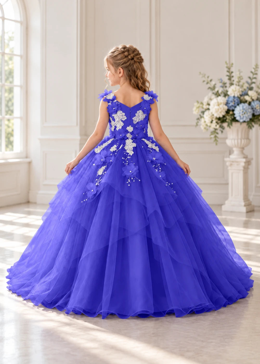 Rear view of a child wearing a royal blue flower girl dress with a V-neckline, floral shoulder appliques and lace and flower decoration across the bodice and hips.