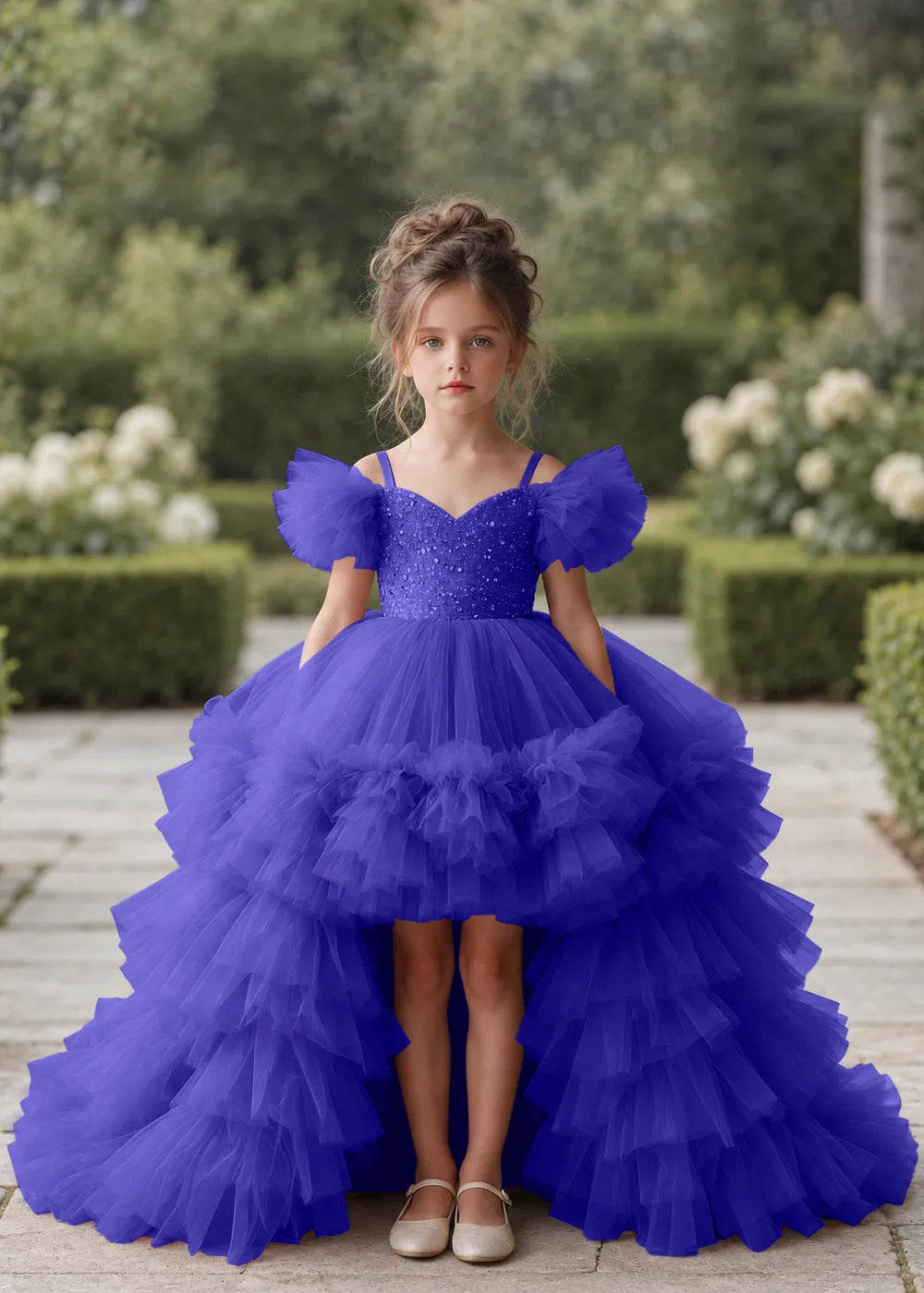 Front view of a child wearing a royal blue flower girl dress with a V-neckline, a sequin-covered bodice and a tiered high-low tulle skirt with off-shoulder sleeve ruffles.