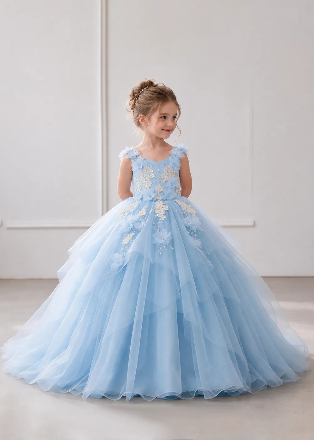 The front view of a child wearing a Sky Blue flower girl dress with a V-neckline, floral shoulder appliques and lace and flower decoration across the bodice and hips.
