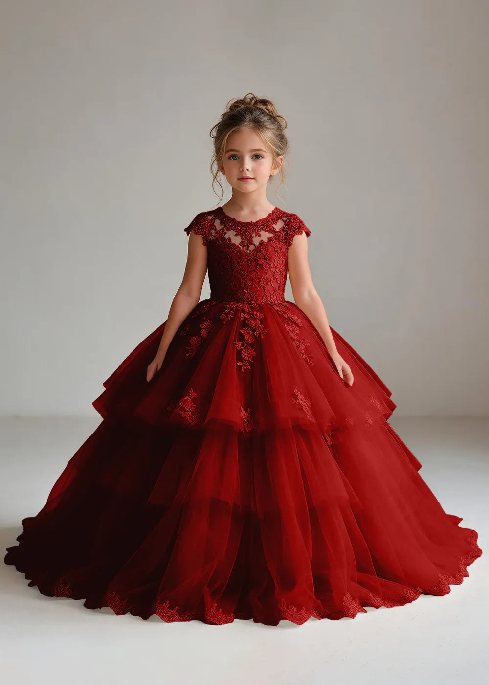 Front view of a child wearing a wine red flower girl dress with a sheer lace illusion neckline, cap sleeves and a tiered cake-style tulle skirt with a lace-trimmed hem.