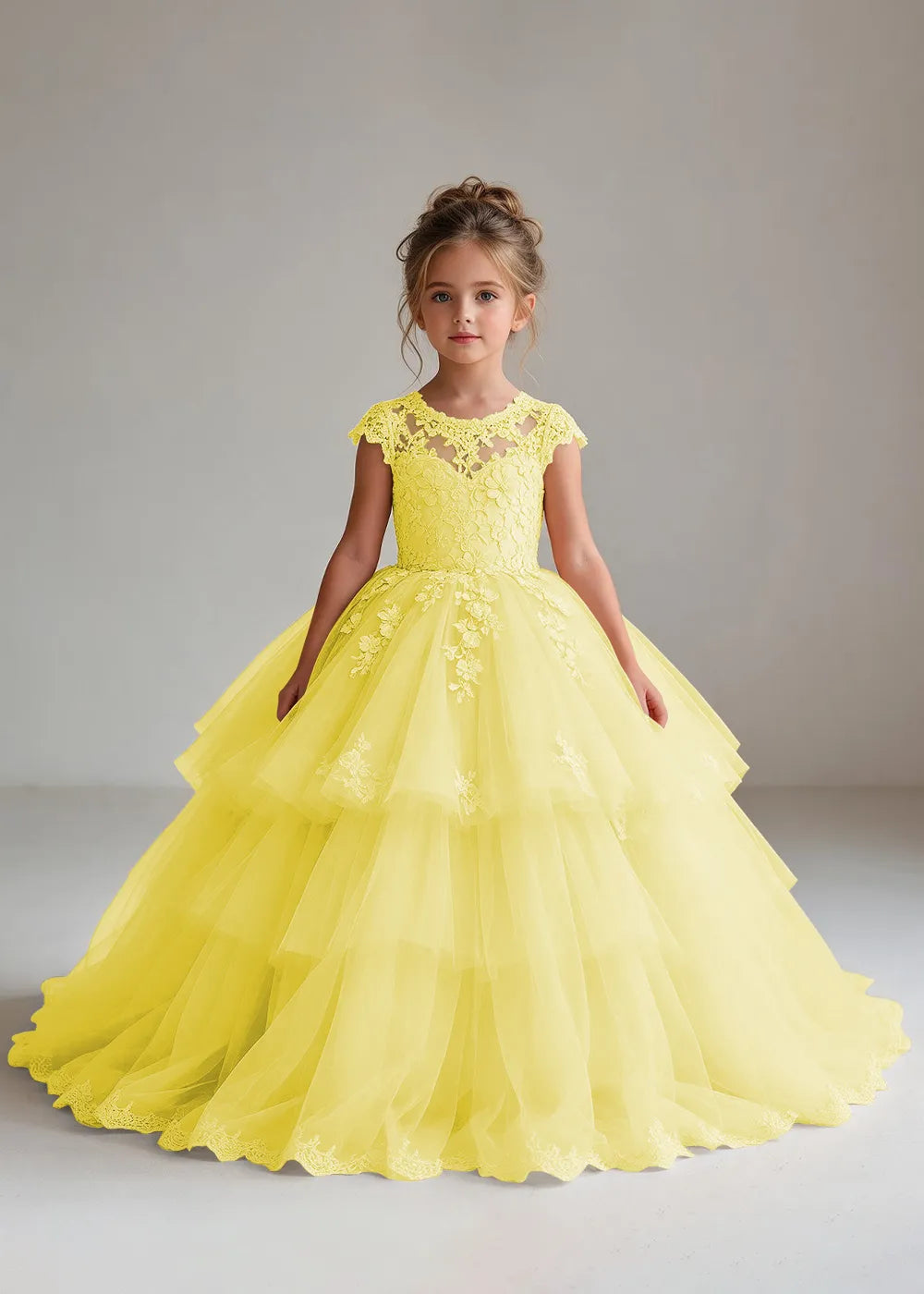 Front view of a child wearing a yellow flower girl dress with a sheer lace illusion neckline, cap sleeves and a tiered cake-style tulle skirt with a lace-trimmed hem.